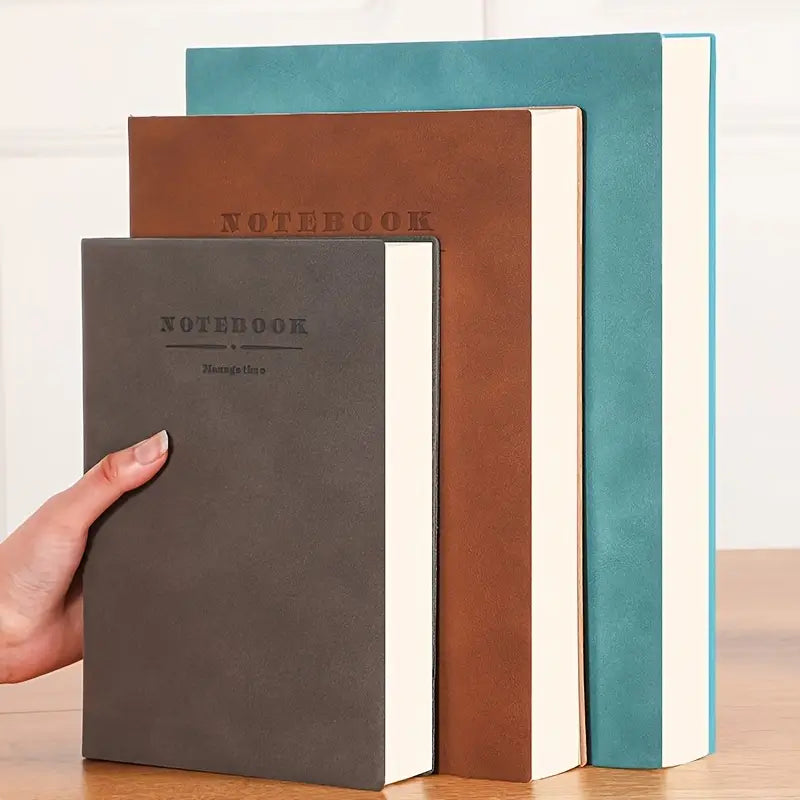 Four notebooks in different colors (gray, brown, blue, and green) on a wooden surface. Bullet journal A5, academic planner, business notebook