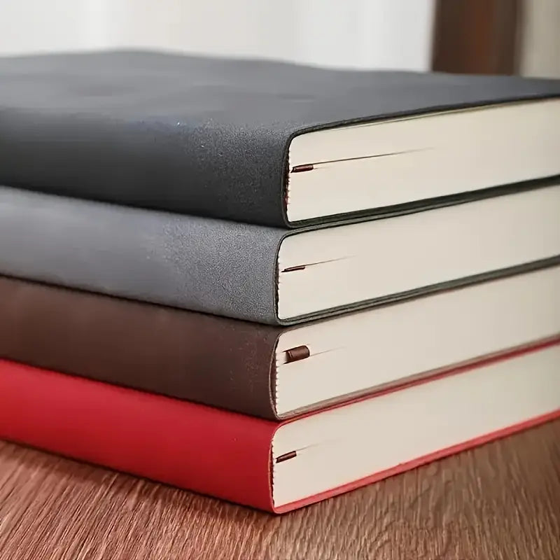 Stack of three leather-bound books in black, gray, and red on a wooden surface - academic planner, business notebook, luxury notebook