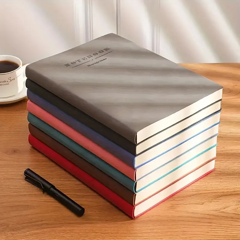 Stack of leather-bound notebooks in various colors on a wooden surface with a pen and coffee cup. Square grid notebook, professional writing notebook, soft leather journal
